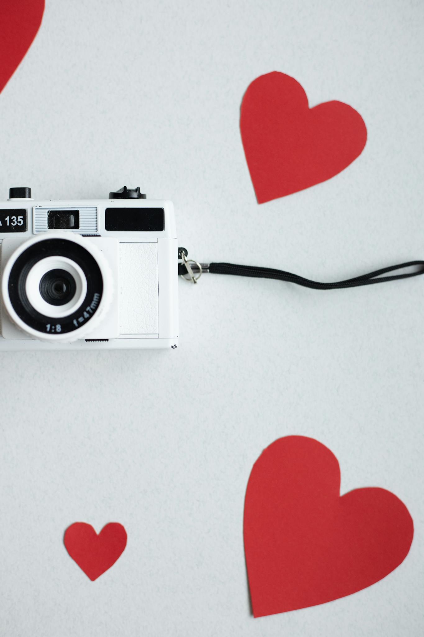 Top view paper cutout of red hearts on white background with old fashioned photo camera during valentines day holiday celebration