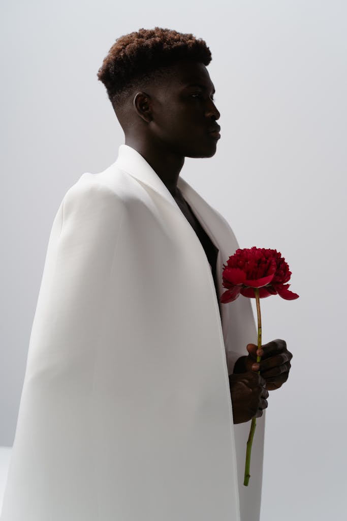 A Man Draped in White Fabric Holding a Red Flower